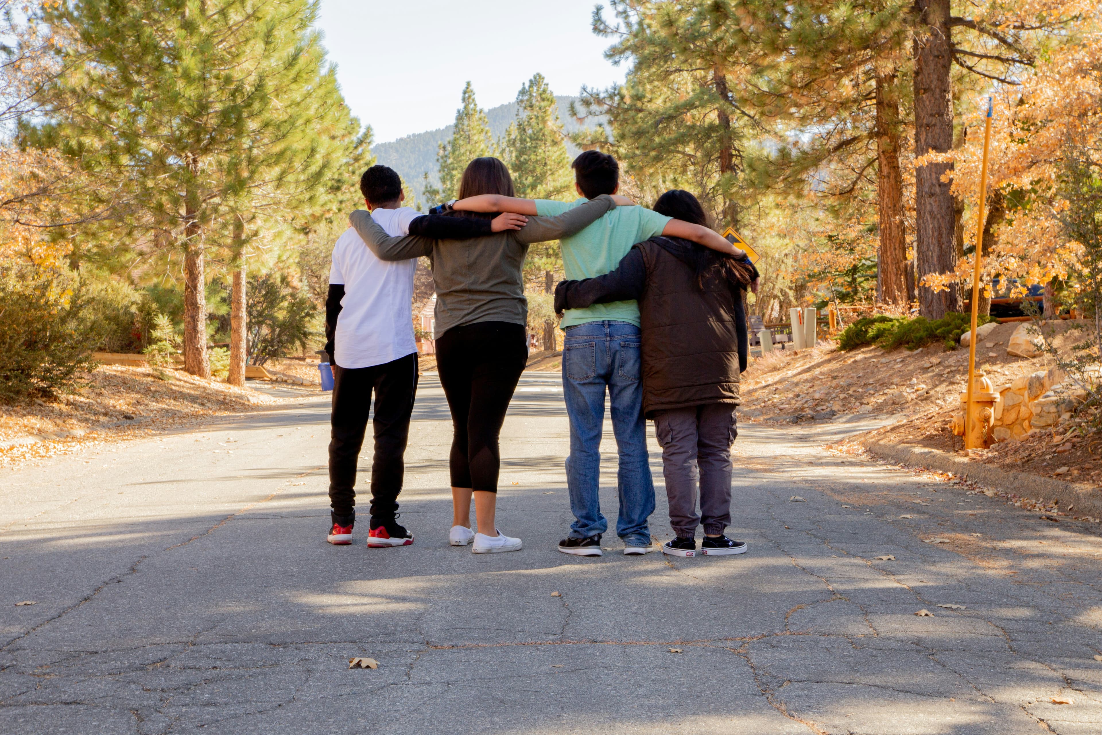 A group of four friends standing together with their arms around each other on a road, symbolising support and togetherness during difficult times