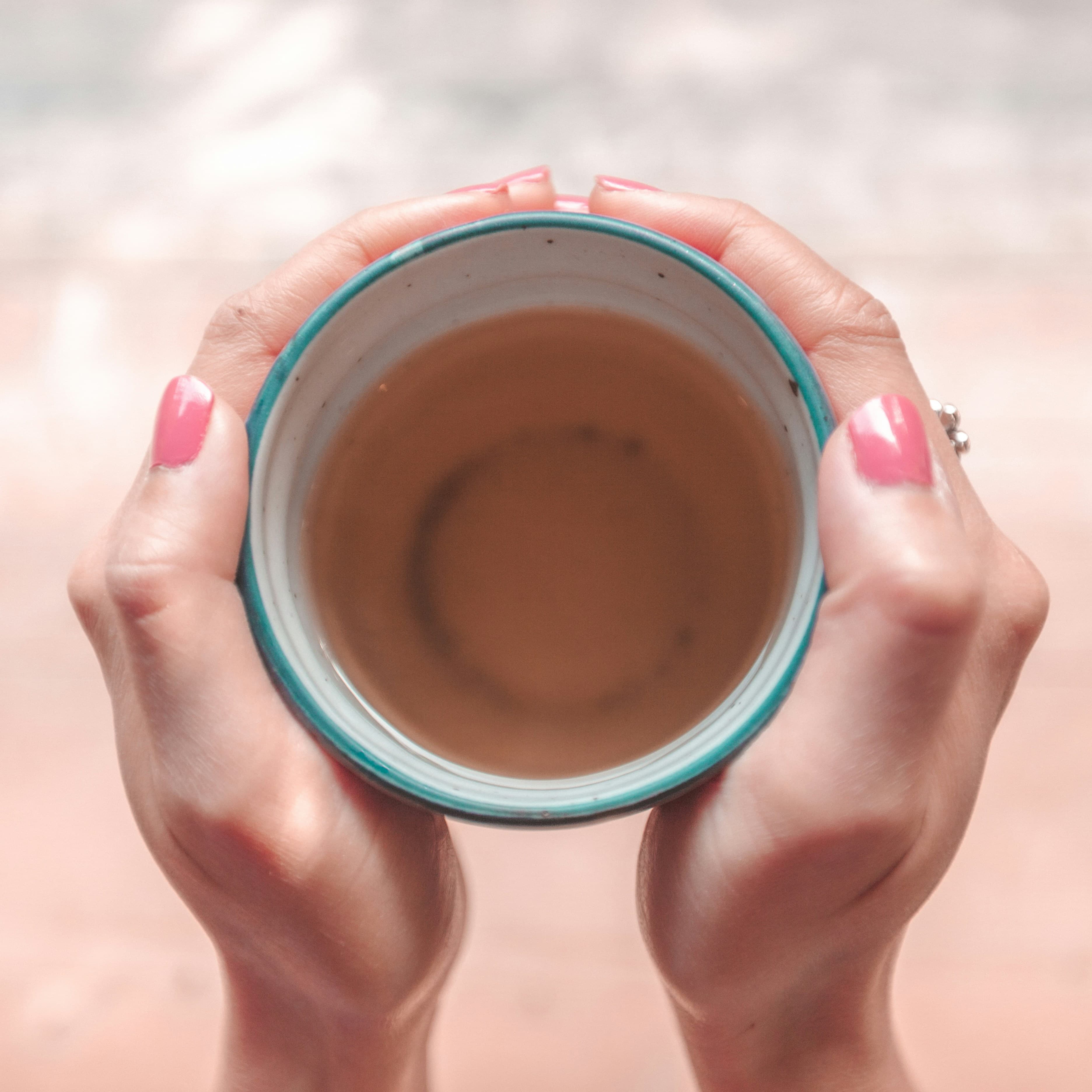 Hands gently cradling a warm cup of tea, seen from above